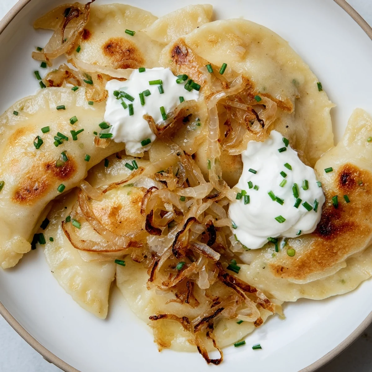 Golden brown Polish pierogi dumplings, crisped after boiling, with caramelized onions awaiting.