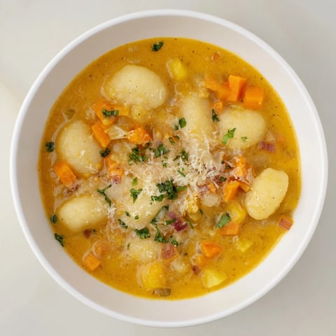 Creamy bowl of Savory Butternut Squash Gnocchi Soup, garnished with fluffy Parmesan cheese and herbs.
