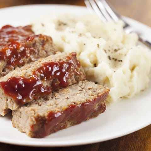Comforting Classic Meatloaf & mashed potatoes garnished with fresh parsley and savory glaze.  