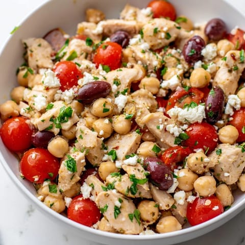 Freshly tossed Mediterranean Chickpea Chicken Salad in a glass bowl, featuring crisp cucumber, red onion, and briny Kalamata olives.
