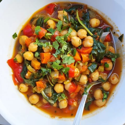 Close-up of Spicy Chickpea Stew in a rustic pot, featuring tender chickpeas and wilted spinach in a rich tomato broth.
